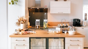 A modern kitchen with white cabinetry, a wooden countertop, and a glass-fronted bar area. - Le Hameau de Céline (Landes-le-Gaulois)