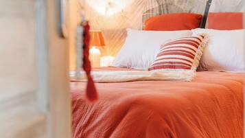 Un dormitorio con cama, almohadas, una mesita de noche y una pared con diseño de hojas.