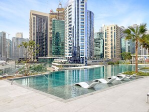 A modern hotel with a pool area, surrounded by high-rise buildings and palm trees. - Peninsula 3 - 1320 1BD (Dubai)