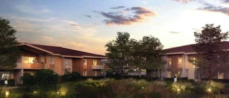 A modern hotel with a row of rooms, a landscaped garden, and a body of water.