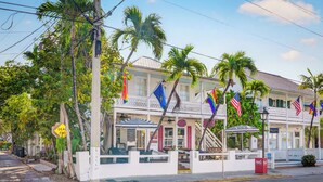 A white building with a balcony, palm trees, and flags. - QUIET POUR ~ On Duval St, Adult Only, Adjoining Rum Bar and Near Beach! (Key West)