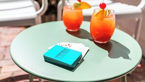 A green table with two drinks, a blue card, and a chair in the background. - AFTER HOURS ~ On Duval St, Adult Only, Adjoining Rum Bar & Nearby Beaches! (Key West)