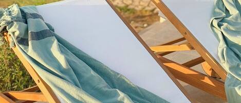A sun lounger with a light blue towel draped over it, positioned on a patio with a garden in the background.