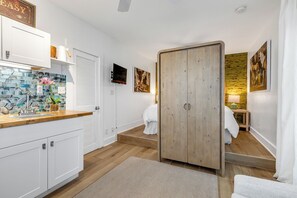 Una habitación de hotel moderna con un armario de madera, un baño con ducha y una cocina con salpicadero de azulejos.