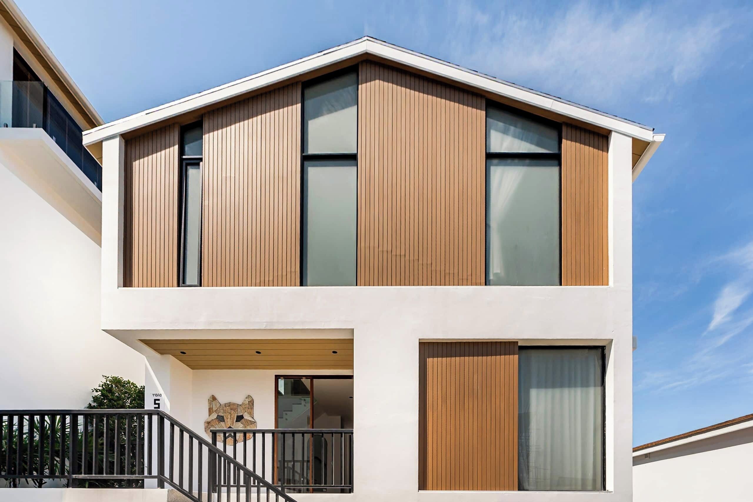 A modern two-story building with a flat roof, large windows, and a balcony with a black railing.