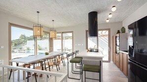 Une cuisine moderne dotée d’un grand îlot central, de tabourets de bar et d’un coin repas offrant une vue sur l’extérieur.
