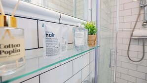A bathroom with a glass shelf holding a bottle of Cotton Poplin, a bottle of FieldDay hair rinse, and a small potted plant. - Seaside Getaway in Howth (Howth)