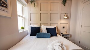 A neatly made bed with white and dark blue pillows, a rolled white towel, and a grey headboard. - Seaside Getaway in Howth (Howth)