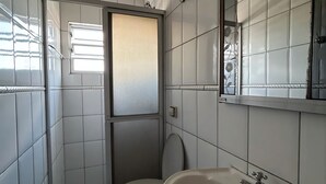 Et lille badeværelse med flisegulv, toilet, vask og et vindue med matteret glas.