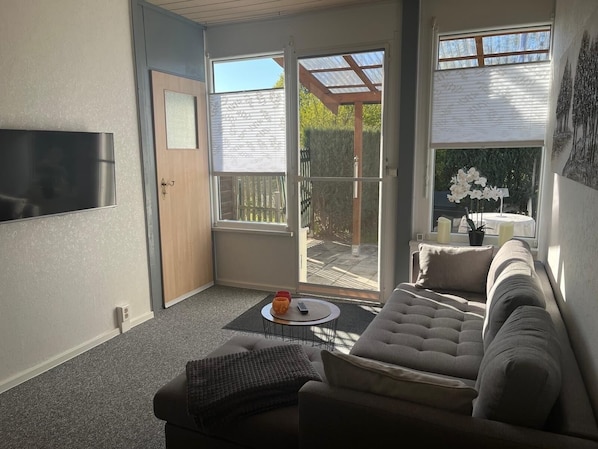 A living room with a sofa, a coffee table, and a TV. There are sliding glass doors leading to an outdoor patio. - Vacation bungalow at the Quitzdorf reservoir in Kollm in beautiful Upper Lusatia (Quitzdorf am See)