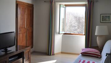 Una habitación con televisión, mueble de madera, ventana con cortinas y una cama con almohada.