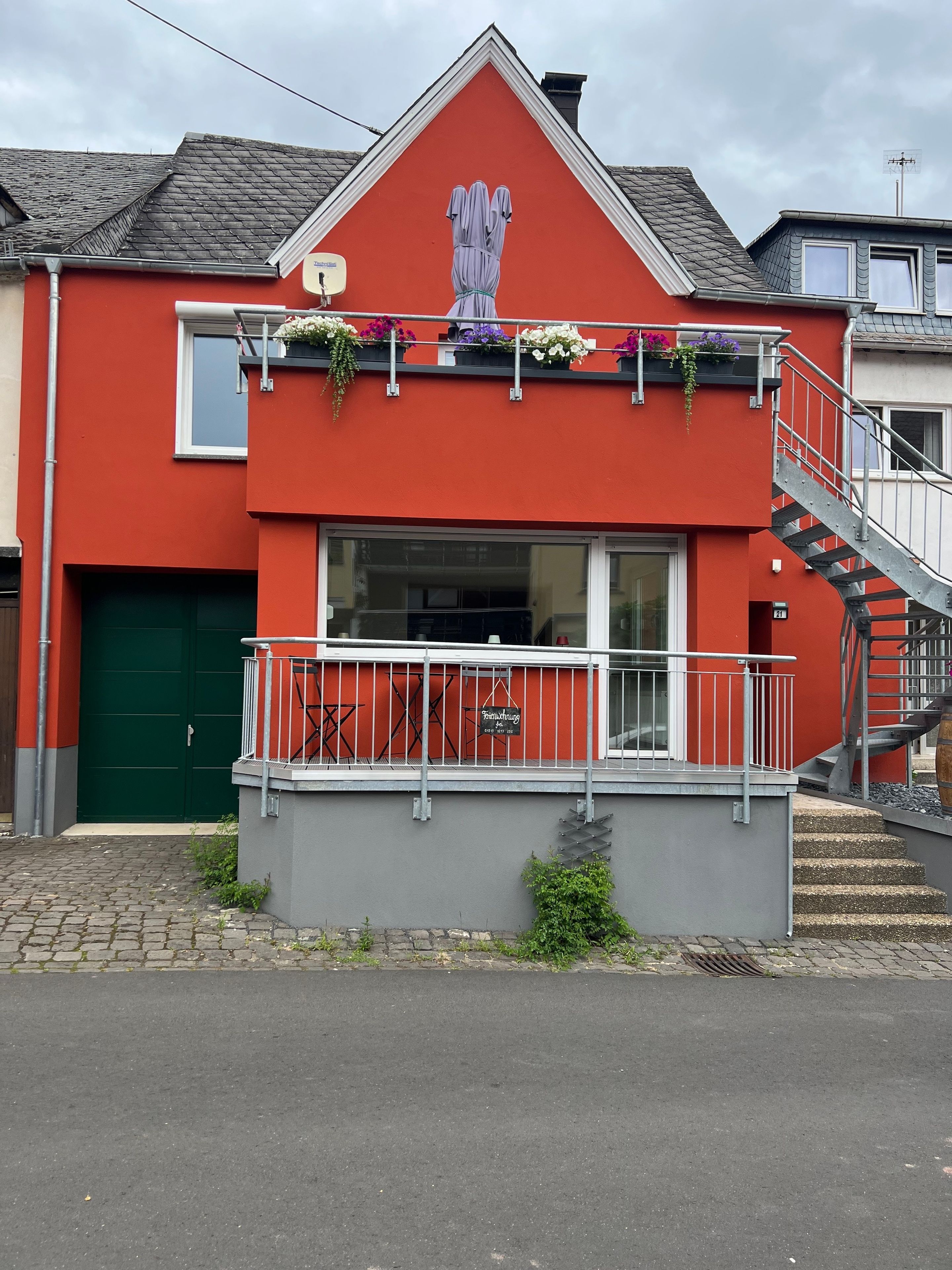 Ein rotes Gebäude mit einer grünen Tür, einem Balkon voller Blumen und einer Treppe.