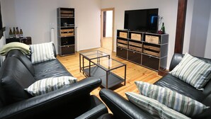 Una sala de estar con un sofá de cuero negro, almohadones a rayas, una mesa de centro de vidrio y piso de madera.