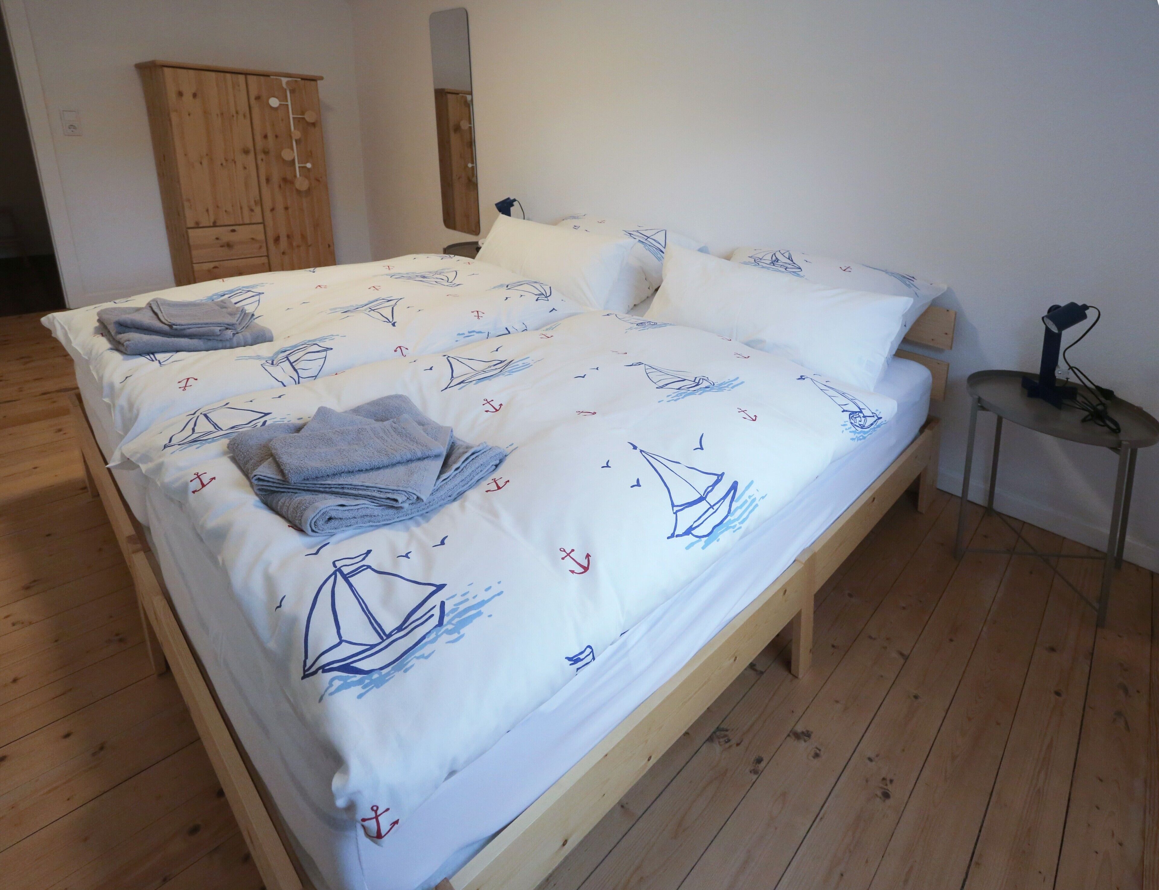 Un lit avec une couvre-lit à motifs nautiques, une armoire en bois et une petite table avec une lampe.