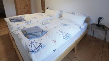 Un lit avec une couvre-lit à motifs nautiques, une armoire en bois et une petite table avec une lampe.