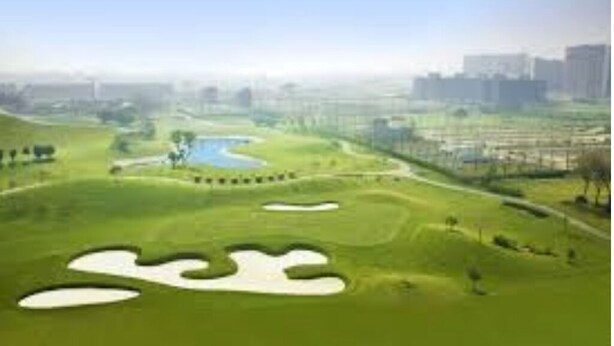 Ein Golfplatz mit Sandbunkern, einem Wasserhindernis und einer Stadtkulisse im Hintergrund.