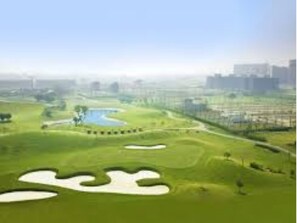 Un campo de golf con búnkeres de arena, un estanque y un horizonte urbano al fondo.