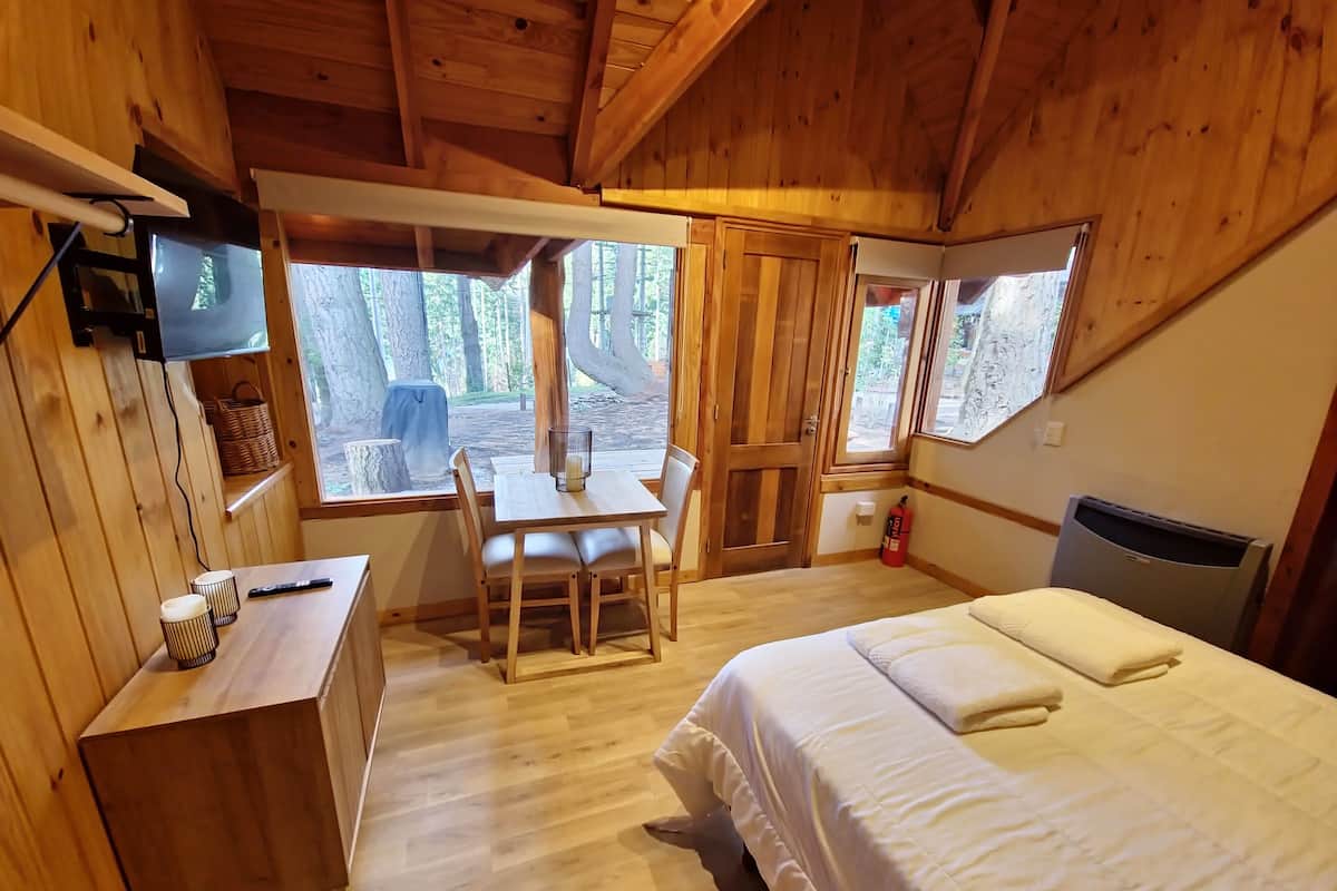 Una habitación de cabaña de madera con una cama, un escritorio, una silla y un televisor montado en la pared.