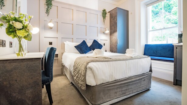A modern bedroom with a large bed, a desk, and a window with a view of greenery. - Charming Suite at the Marina (Howth)