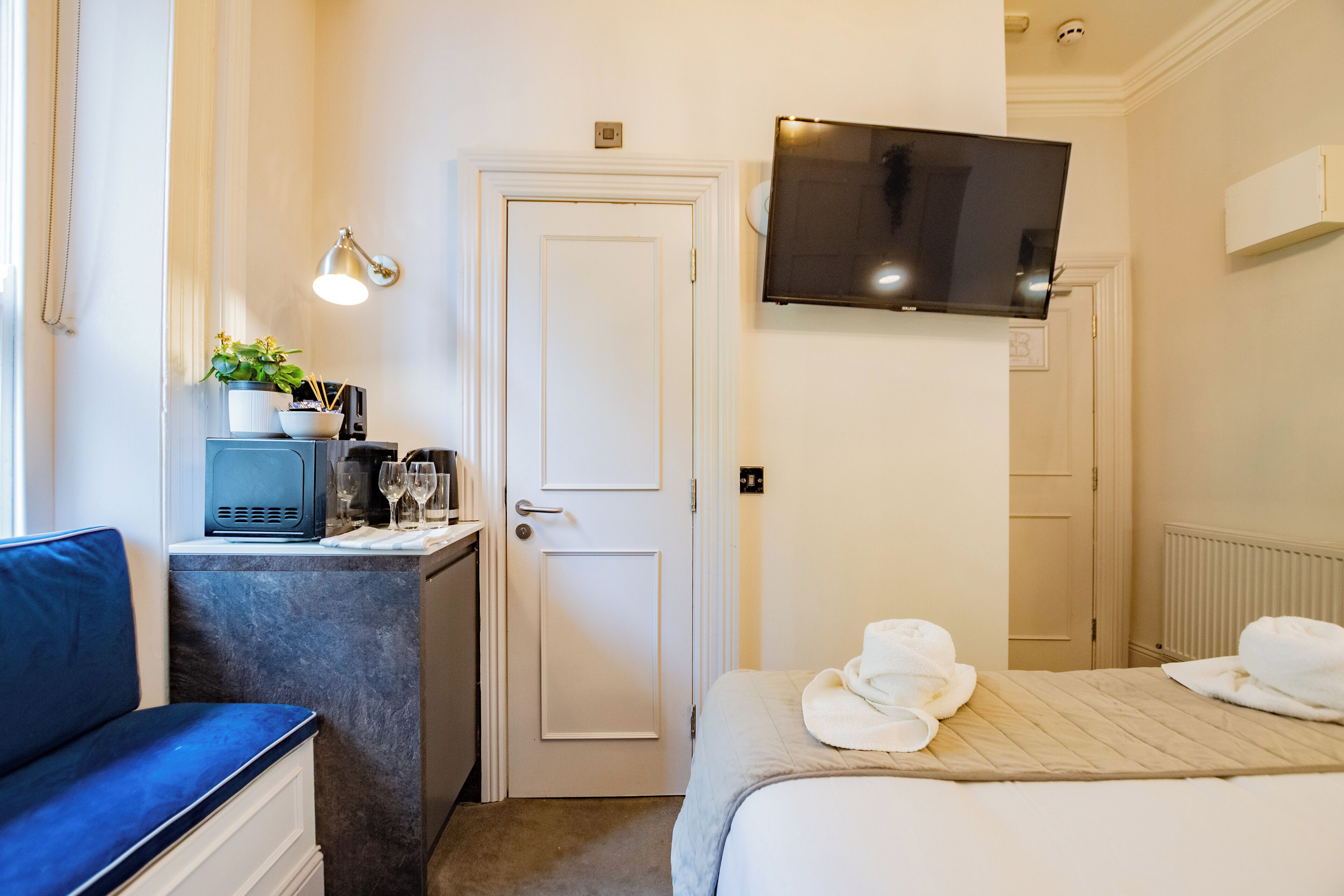 A hotel room with a bed, a desk with a computer, a TV mounted on the wall, and a window.
