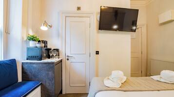 A hotel room with a bed, a desk with a computer, a TV mounted on the wall, and a window.