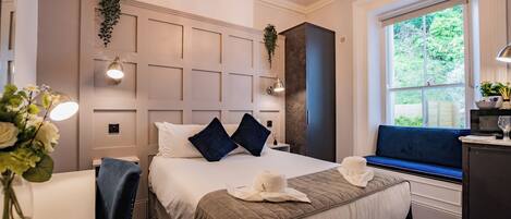 Habitación de hotel con una cama grande, zona de estar junto a la ventana, un escritorio y una araña.