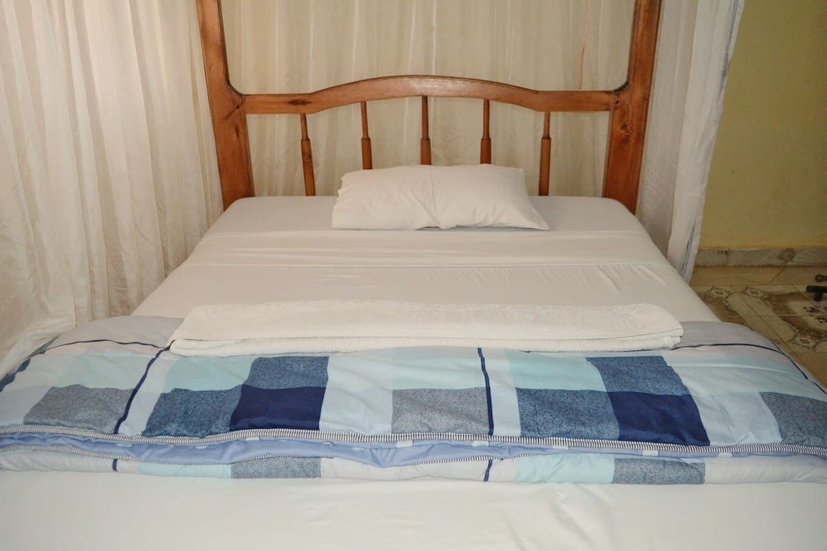 A single bed with a wooden headboard, white bedding, and a blue and white checkered blanket.