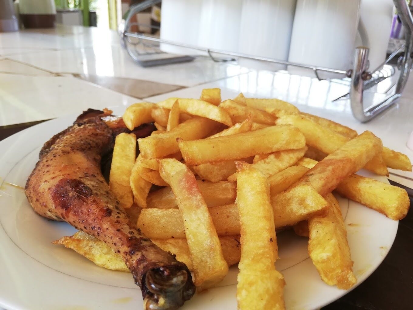 Un plato con un muslo de pollo asado y una porción de papas fritas doradas.