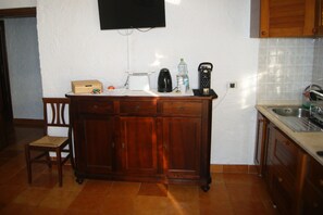 Een keuken met een houten kastje, een broodrooster, een waterkoker, een fles en een telefoon.