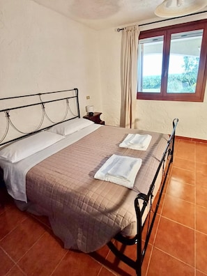 Ein Einzelbett mit Kopfteil, ein Nachttisch mit Lampe und ein Fenster mit Vorhängen.