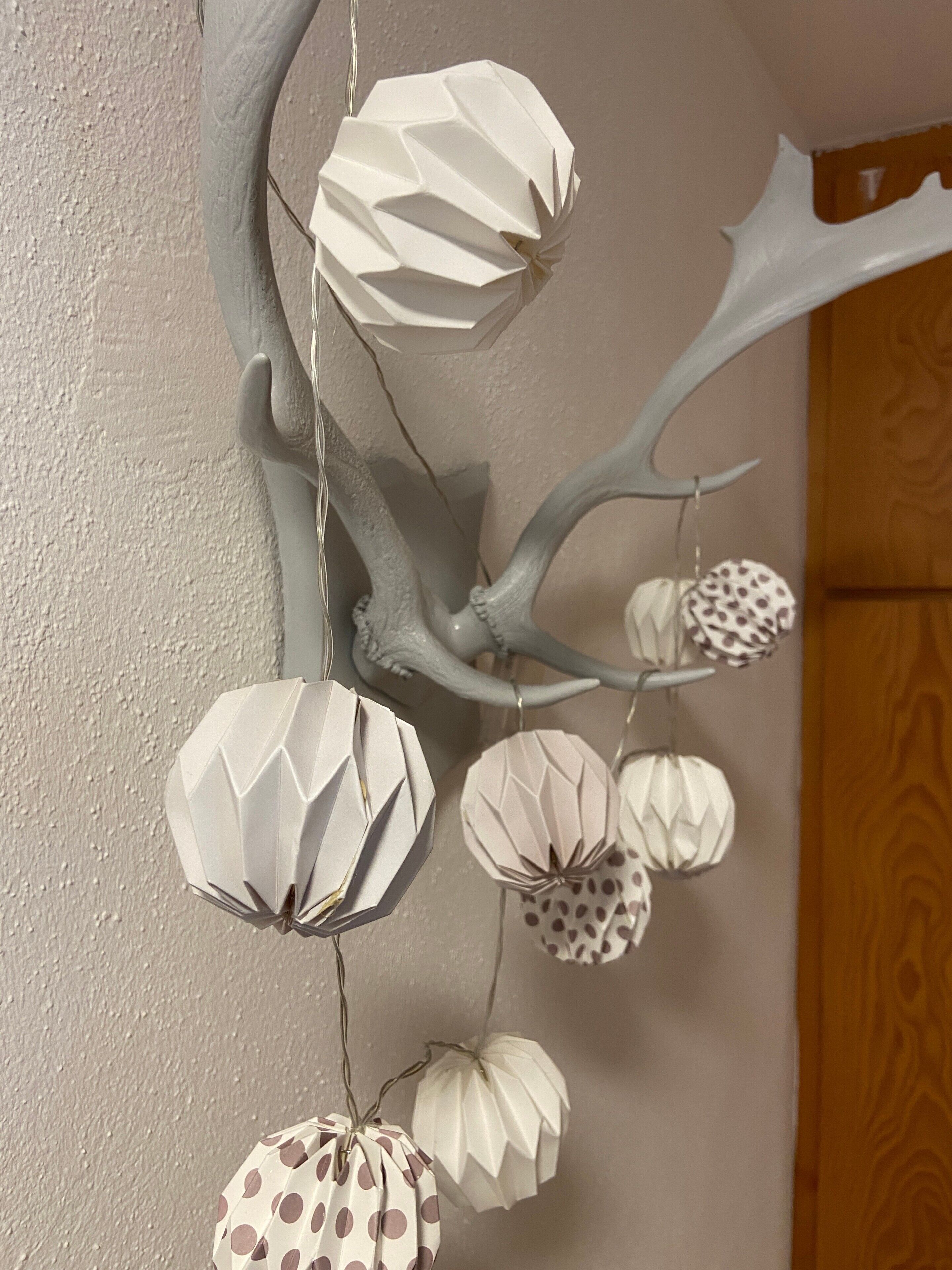 Una pieza decorativa de pared con farolillos de papel geométricos y estructuras similares a astas.