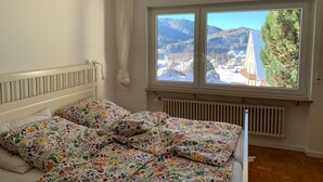 A bedroom with a bed, a window with a view of mountains, a radiator, and a hanging light fixture. - Apartment 'Lichtblick unter der Buche' with Terrace, Great Views and Wi-Fi (Titisee-Neustadt)