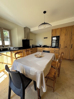 Une cuisine avec des meubles de rangement en bois, une table à manger avec des chaises, un luminaire suspendu et une fenêtre.