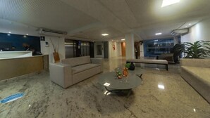 A modern lobby with a reception desk, sofas, a coffee table, and a large window. - Flat 321-GF na praia de Cabo Branco (João Pessoa)