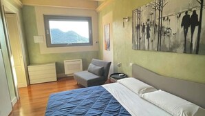 Un dormitorio con una cama grande, una silla, una mesita de noche, una ventana y un cuadro en la pared.