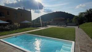 Una piscina rectangular con agua azul cristalina, rodeada por un patio empedrado y una zona verde.
