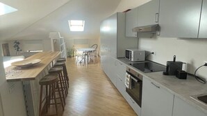 A modern kitchen with grey cabinets, a wooden countertop, and a built-in oven. There are bar stools and a dining table in the background. - Cozy Studio in the Heart of Franciacorta - Base for Lake Iseo (Passirano)