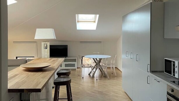 A modern kitchen with a central island, a dining area with a round table, and a skylight. - Cozy Studio in the Heart of Franciacorta - Base for Lake Iseo (Passirano)