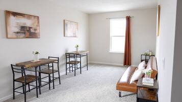 A modern living room with a wooden dining table, two chairs, a brown leather sofa, and a small side table.