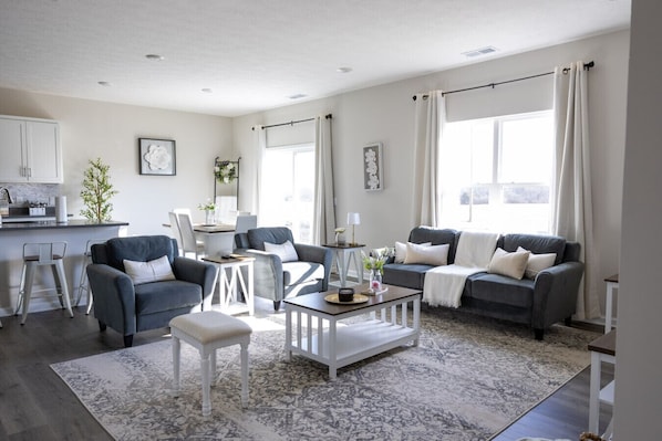 A modern living room with a grey sofa, a white coffee table, and a dining area with a white table and chairs.