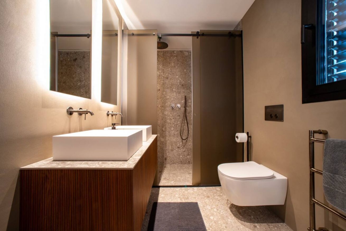 A modern bathroom with a wooden vanity, a white sink, a shower, and a toilet.