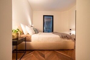 A bedroom with a bed, bedside table, lamp, and a window with blinds.