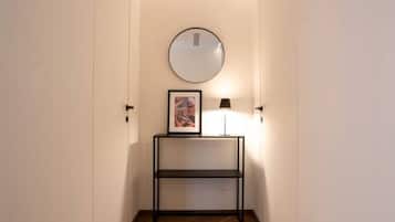 A hallway with a framed picture on a console table, a round mirror on the wall, and a floor lamp.
