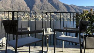 Eine Terrasse mit zwei Stühlen und einem Tisch mit Blick auf einen See und Berge.