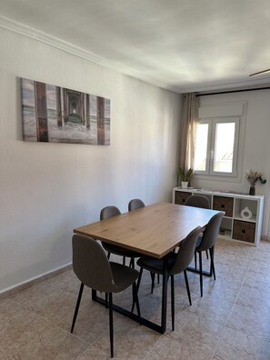 A dining area with a wooden table and four chairs, a white cabinet with storage, and a painting on the wall.