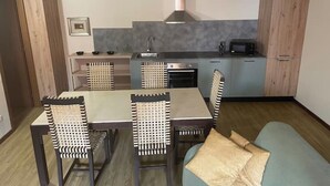 A compact kitchen with a dining table and chairs, a microwave, and a stove. - Villa Valle Franciacorta - Green Apartment with Pool and Garden (Rodengo-Saiano)