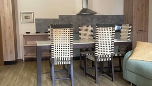 A dining area with a table and chairs, a sofa, and a kitchen area in the background. - Villa Valle Franciacorta - Green Apartment with Pool and Garden (Rodengo-Saiano)
