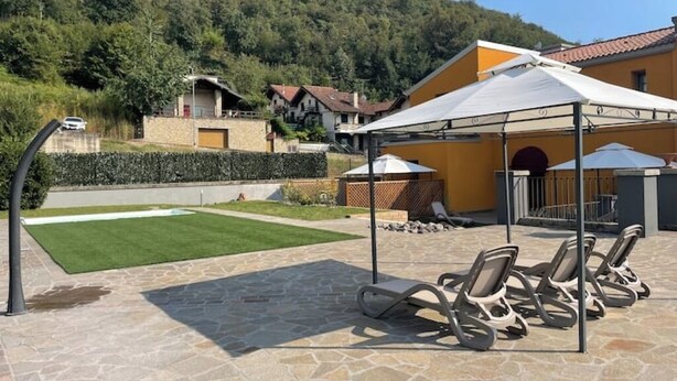A patio area with stone flooring, outdoor seating, and a white canopy. - Villa Valle Franciacorta - Green Apartment with Pool and Garden (Rodengo-Saiano)