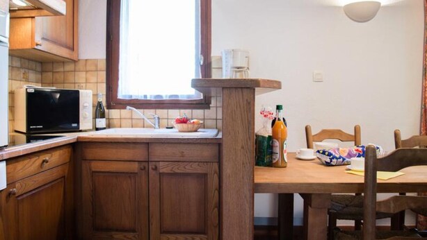 Une cuisine avec des meubles de rangement en bois, un four à micro-ondes, un évier et une table à manger avec des chaises.