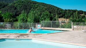 Une piscine avec une personne à l’intérieur, entourée d’une clôture métallique et avec une colline boisée en arrière-plan.